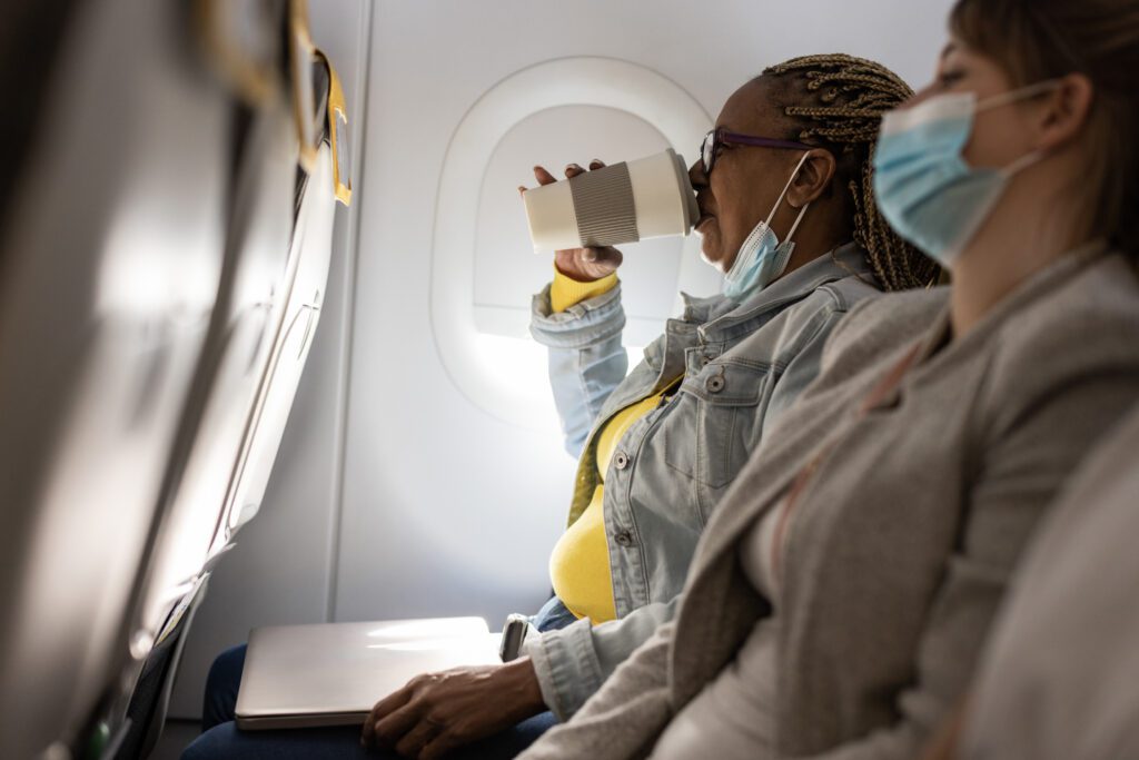 African senior woman drinking coffee traveling on airplane during coronavirus outbreak - Focus on left face